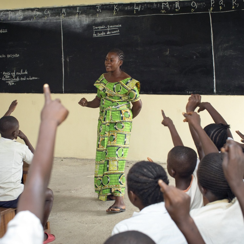 Children raise their hands as teacher Amunazo Belinda gives a lesson at Manua school. DRC