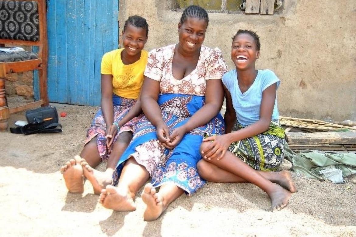 Yankho in front of her house with her mother and her twin sister Pemphero, with their learning materials on the chair behind them. Credit: UNICEF Malawi/2020/Gondwe