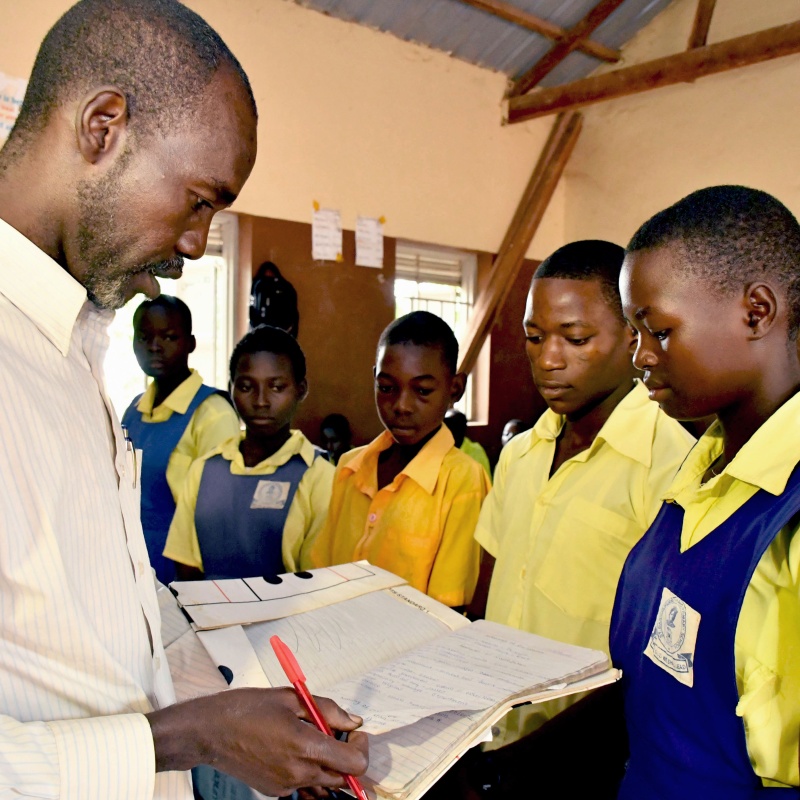 Teacher Adam Gabriel checks the work of his students Moses Justin, Daniel Adam and Salawa Emmanuel during a history lesson at St. Bakhita Primary School. Credit: GPE/Jok Solomon